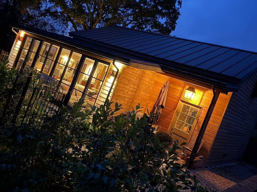 Timber-clad garden building with glazed doors lit at dusk