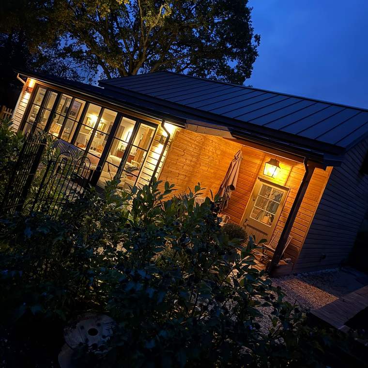 Timber-clad garden building with glazed doors lit at dusk