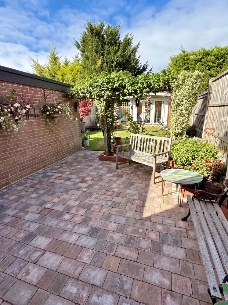 Block paved courtyard patio under a planted pergola with garden benches