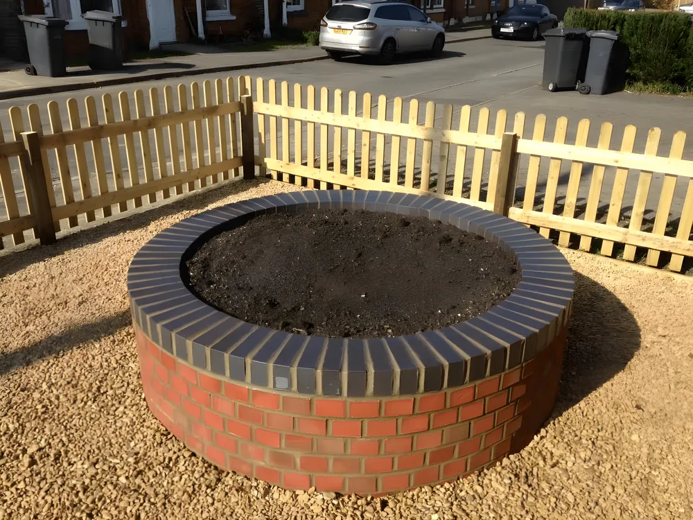 Round brick fire pit with a blue brick coping on a gravel terrace