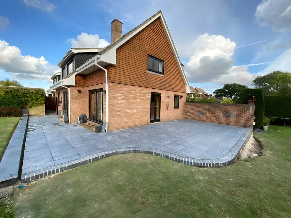 Grey porcelain patio wrapping around a brick house, with a curved lawn edge