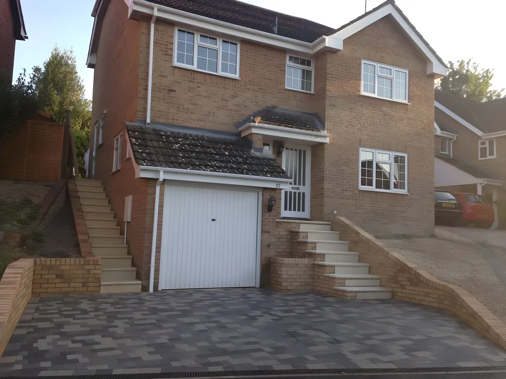 Block paved driveway and steps up to a brick house with a garage