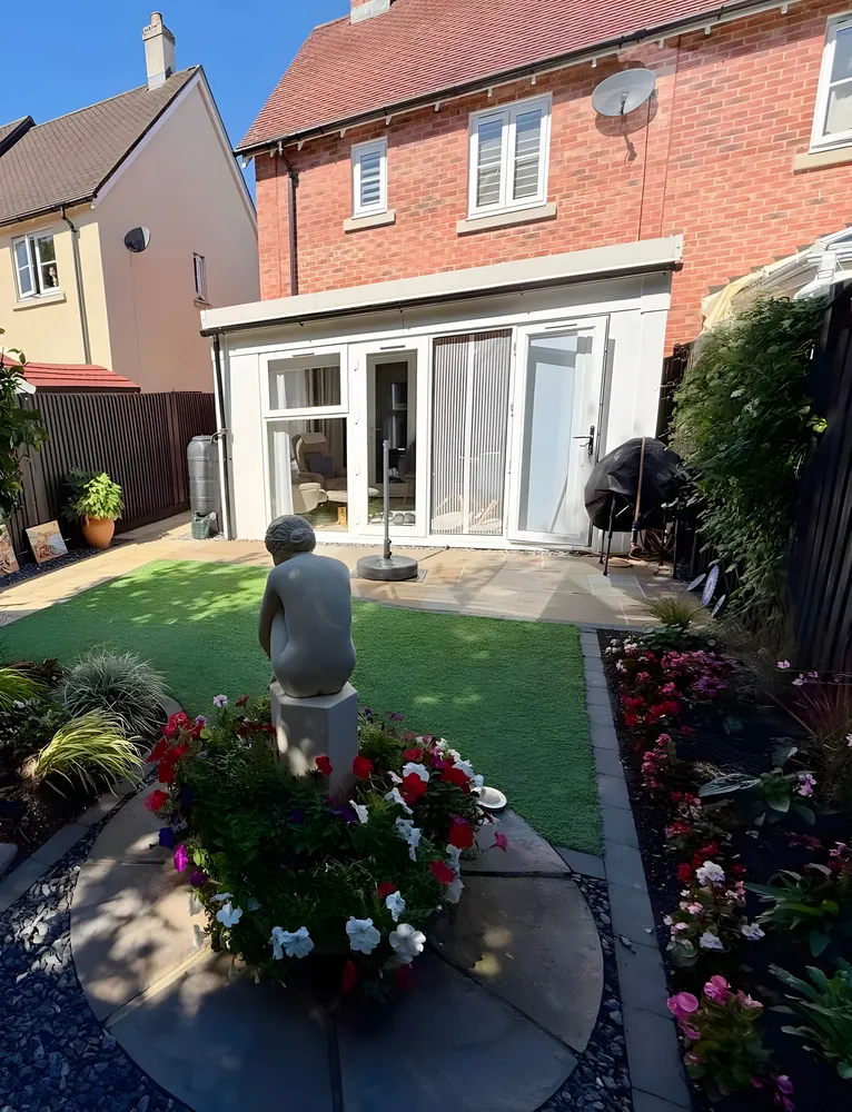 Brick house with a glazed extension above a lawn and a planted statue bed
