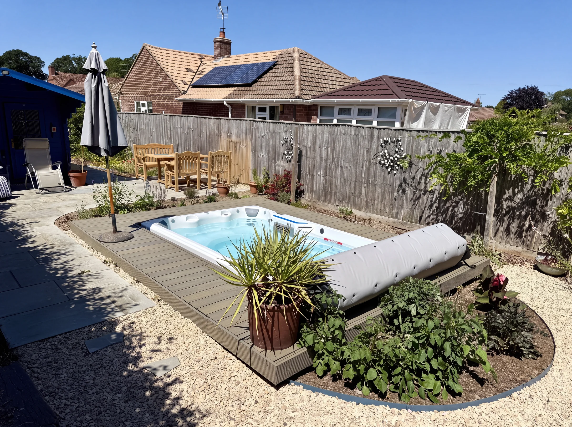Swim spa set into grey composite decking in a back garden, with a gravel and planting surround