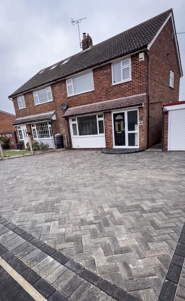 Grey herringbone block paved driveway with a charcoal border in front of a brick semi