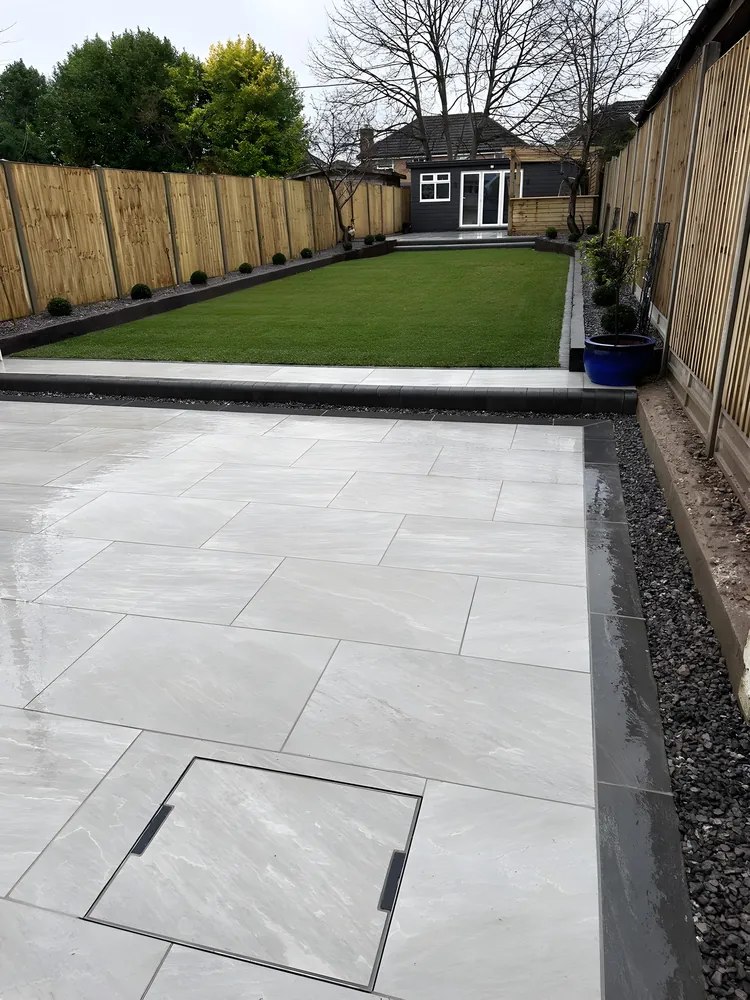 Long porcelain patio with a recessed drain cover and a lawn beyond