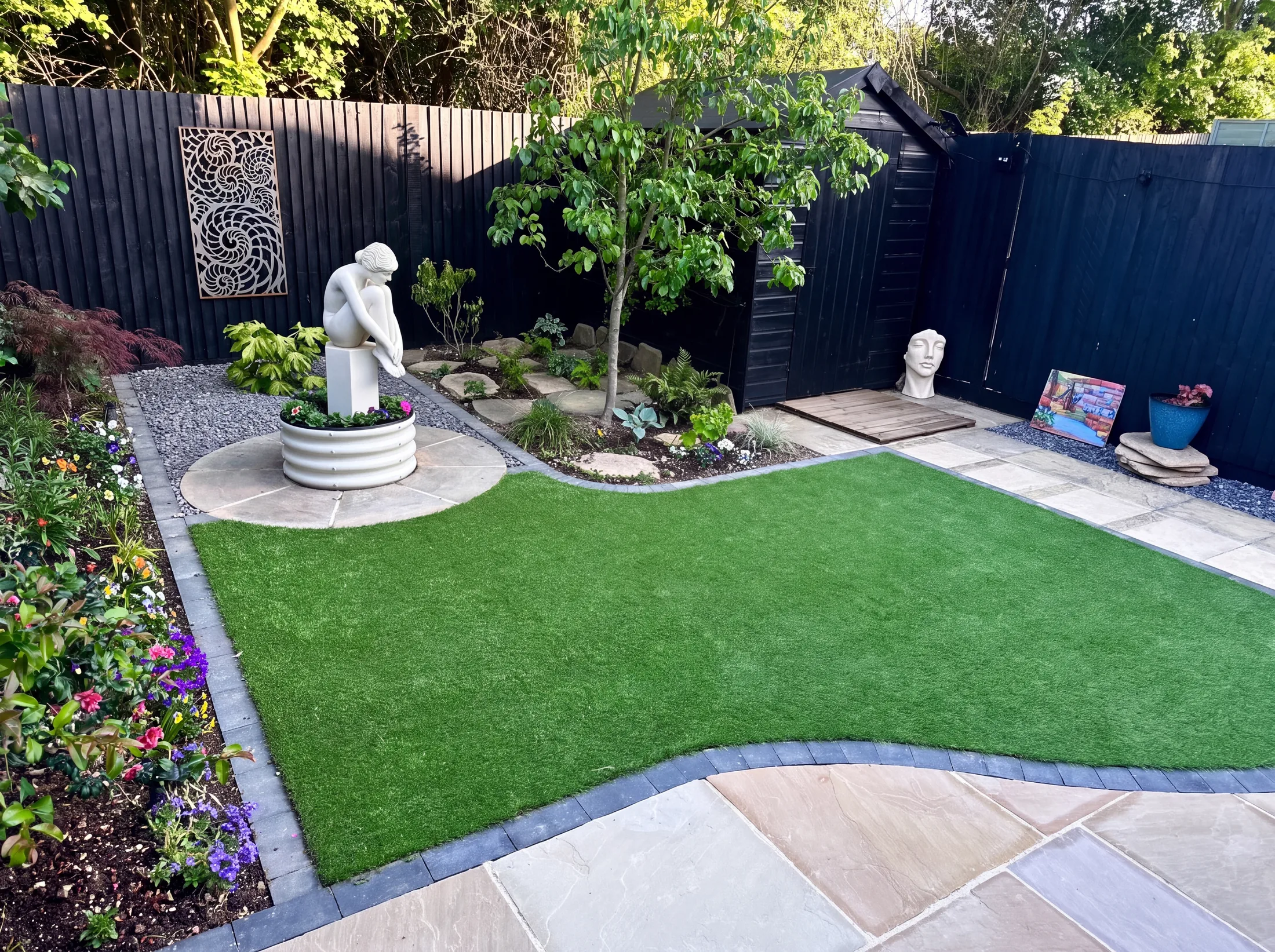 Curved lawn, sandstone paving and a statue set in planted borders
