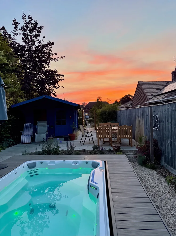 Swim spa with lit water set into composite decking at sunset