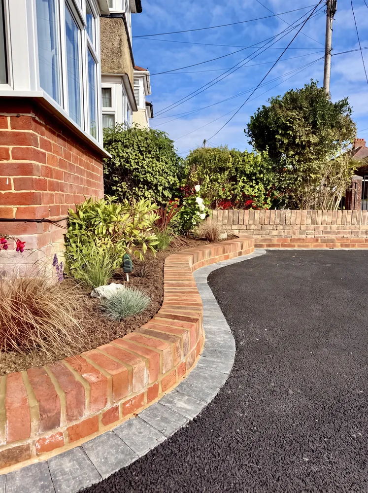 New tarmac driveway with a block edge beside a curved red brick planter