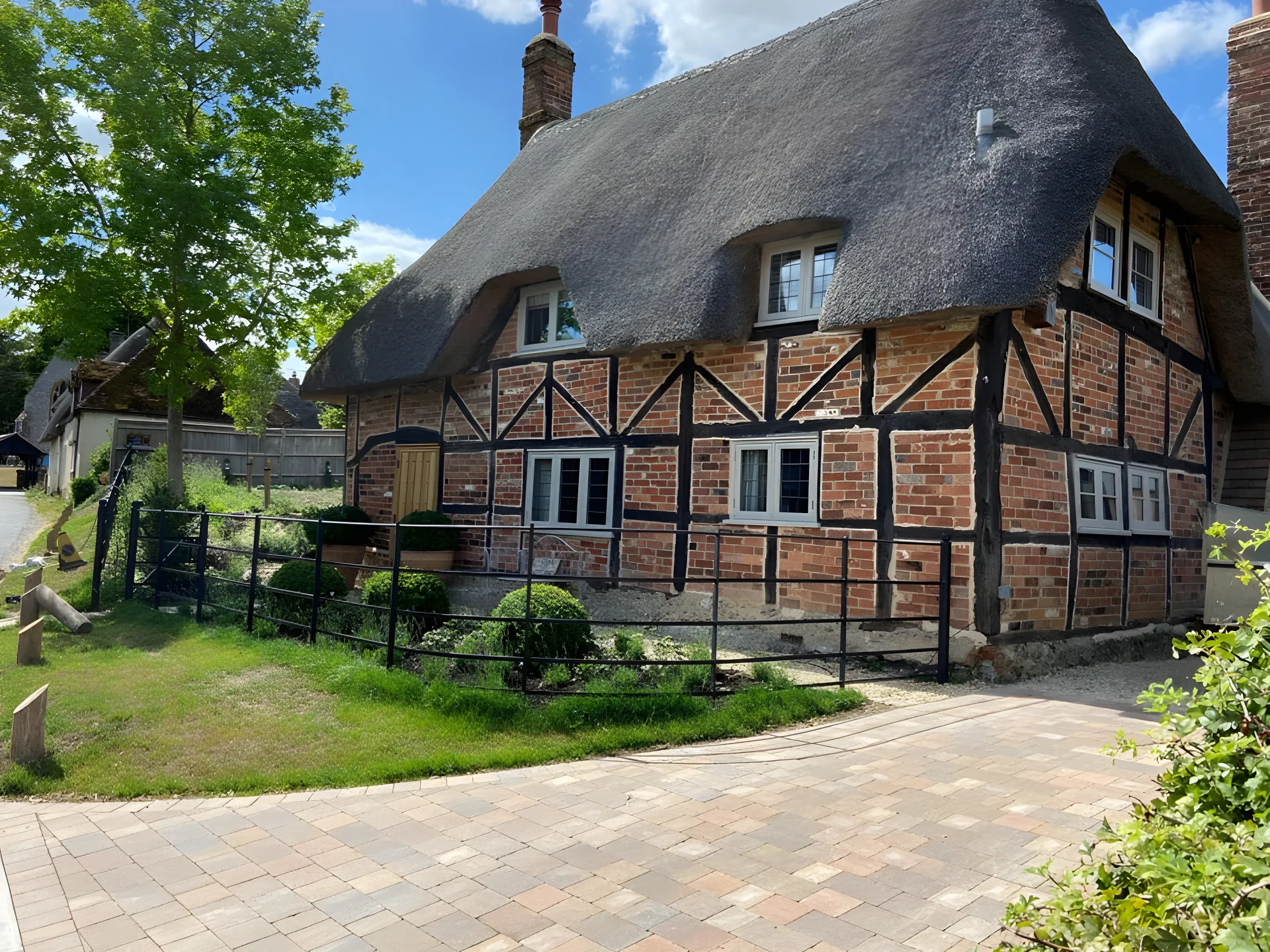 Block paved path and lawn in front of a thatched timber framed cottage